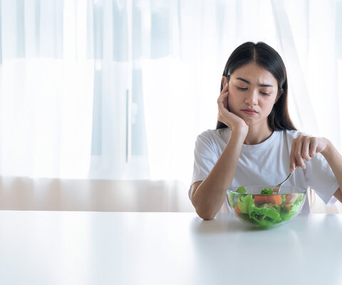 Eine Frau sitzt unglücklich vor einer Schüssel mit Salat.