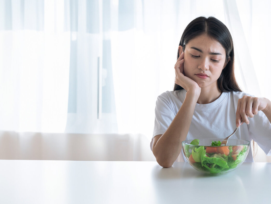 Eine Frau sitzt unglücklich vor einer Schüssel mit Salat.