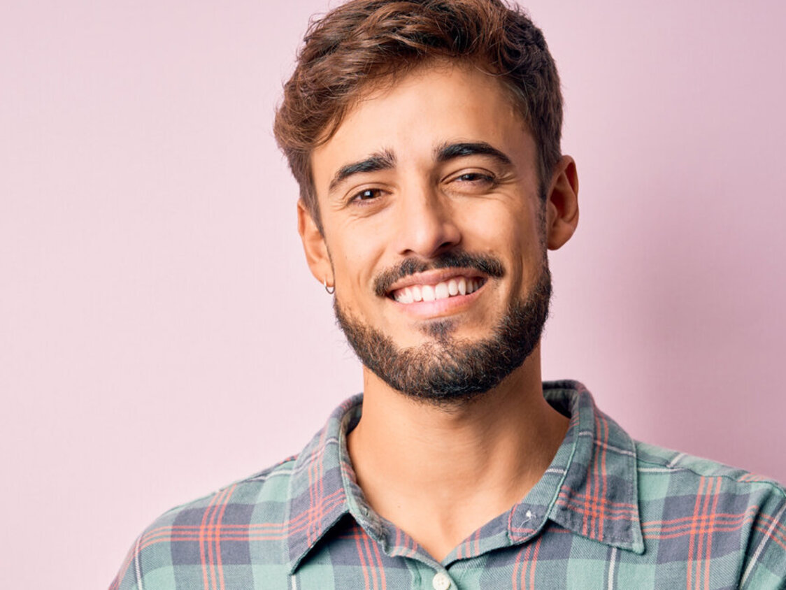 Ein junger Mann mit Bart und kariertem Hemd lächelt freundlich in die Kamera.