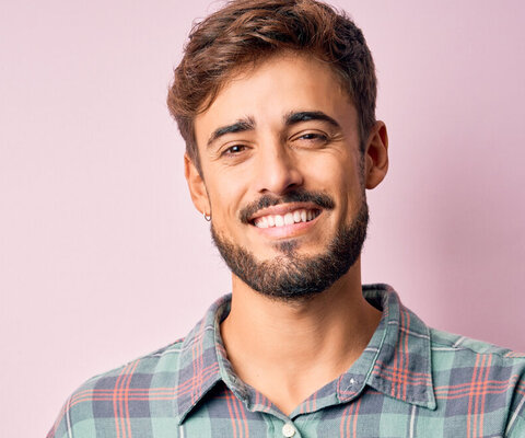 Ein junger Mann mit Bart und kariertem Hemd lächelt freundlich in die Kamera.