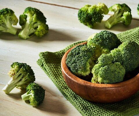 Auf einem Tisch steht eine Schale mit klein geschnittenem Brokkoli.