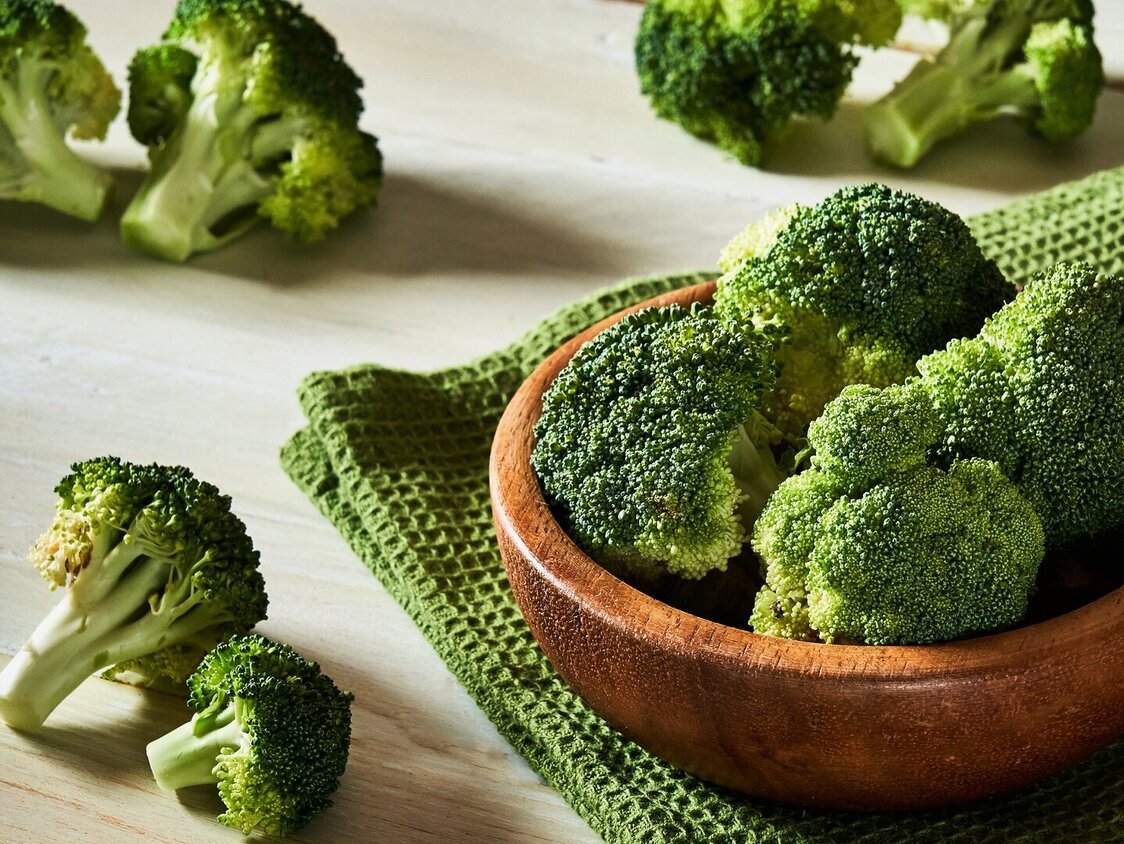 Auf einem Tisch steht eine Schale mit klein geschnittenem Brokkoli.