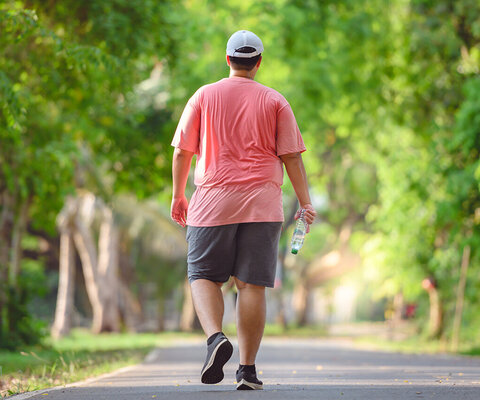 Ein Mann, der verschwitzt in einem Park läuft. Er hält eine Flasche Wasser in der Hand.