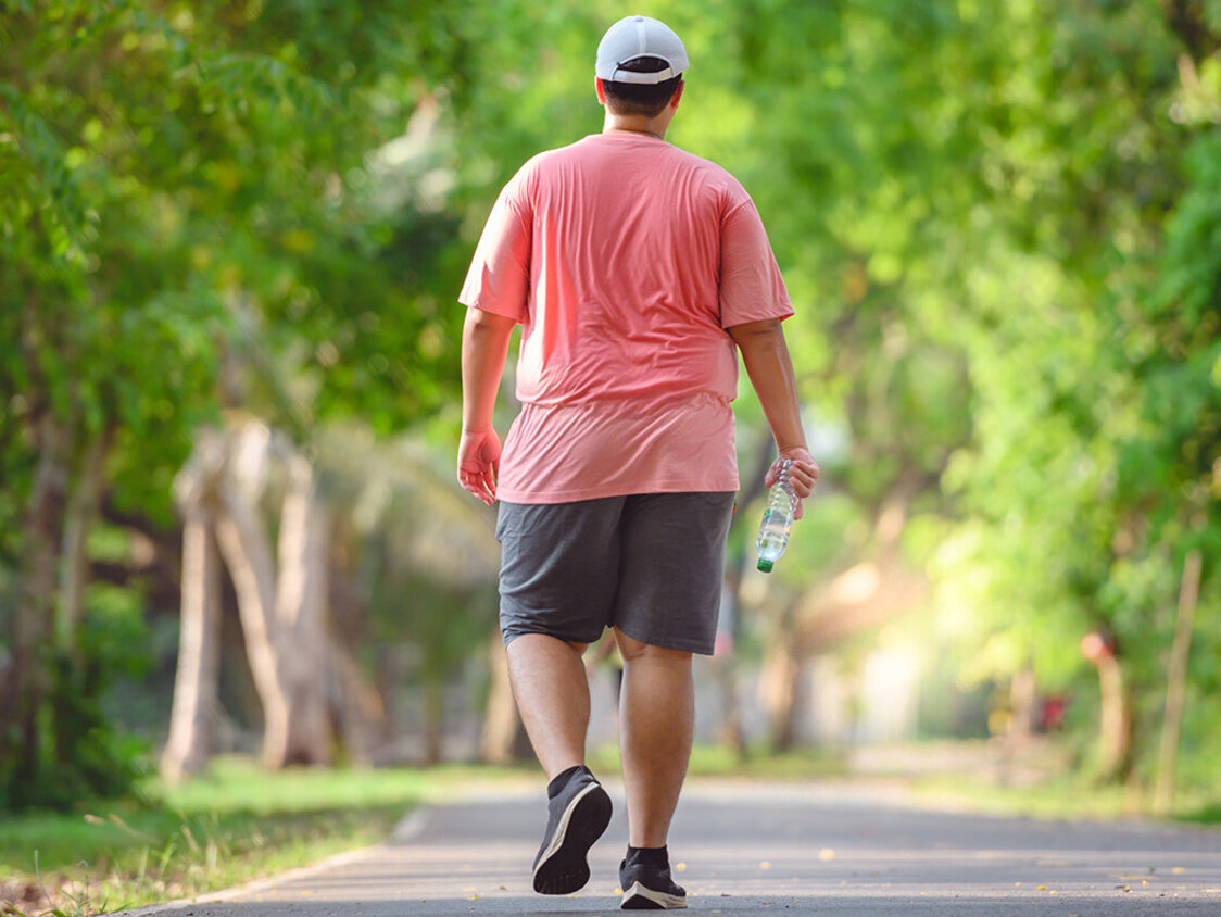 Ein Mann, der verschwitzt in einem Park läuft. Er hält eine Flasche Wasser in der Hand.