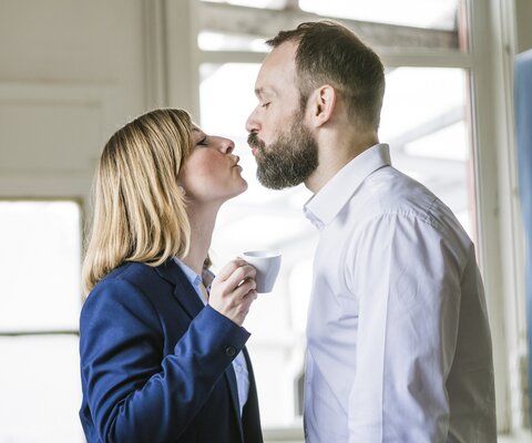 Eine Mann und eine Frau küssen sich am Arbeitsplatz.