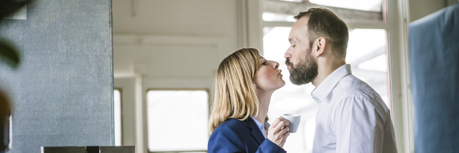 Eine Mann und eine Frau küssen sich am Arbeitsplatz.