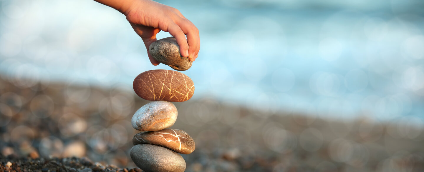 Eine Hand stapelt Steine an einem Strand übereinander.