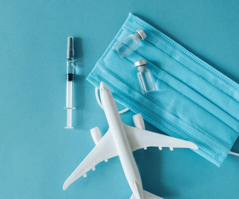 Auf blauem Hintergrund liegt ein Spielzeug-Flugzeug, eine Spritze mit Ampullen und ein Mundschutz.