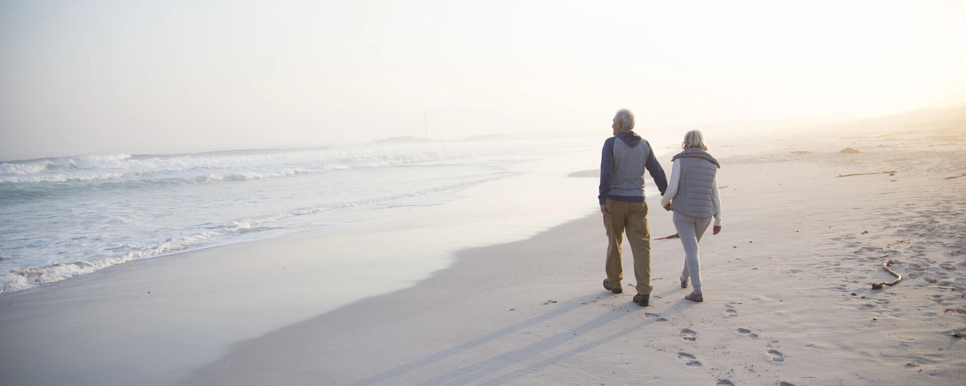  Ein älteres Ehepaar bei einem Strandspaziergang. Die Sonne geht gerade unter.