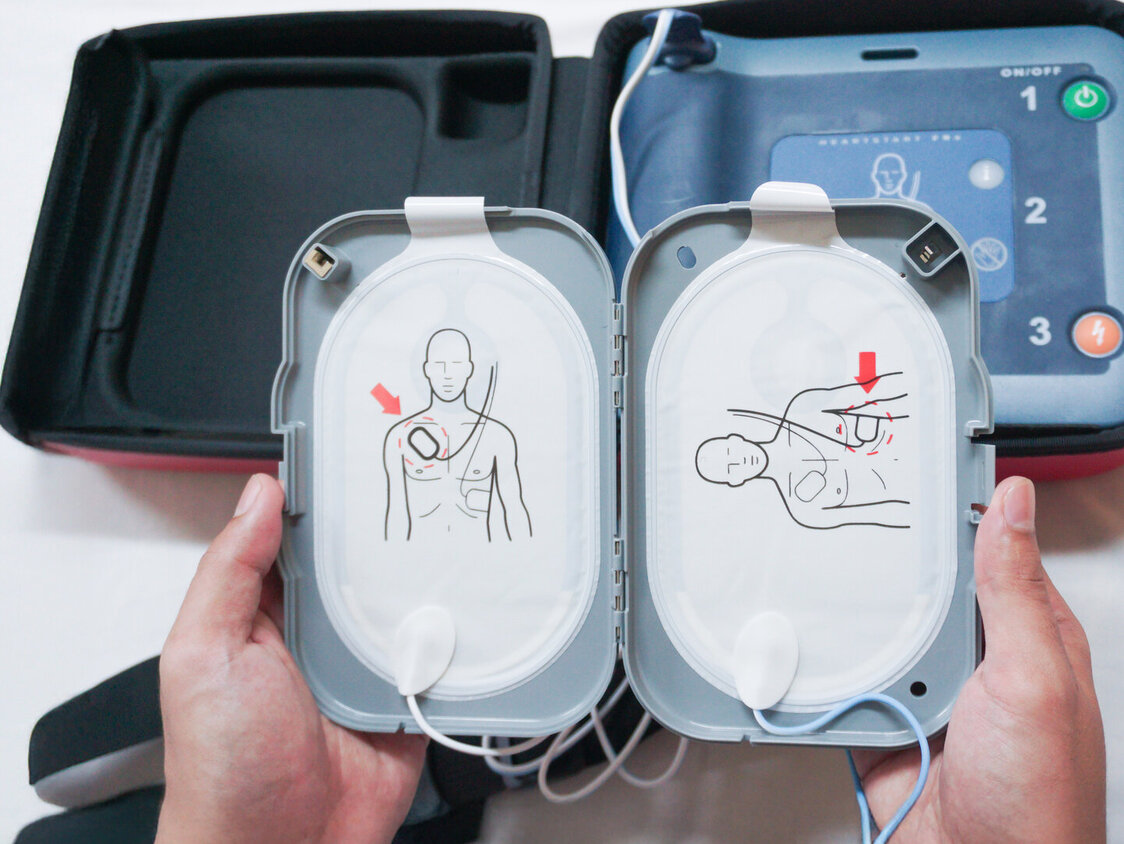 Tragbarer Defibrillator auf einem Holztisch, zwischen zwei Händen.