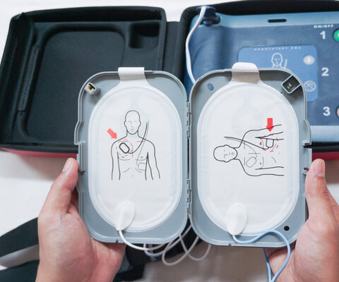 Tragbarer Defibrillator auf einem Holztisch, zwischen zwei Händen.