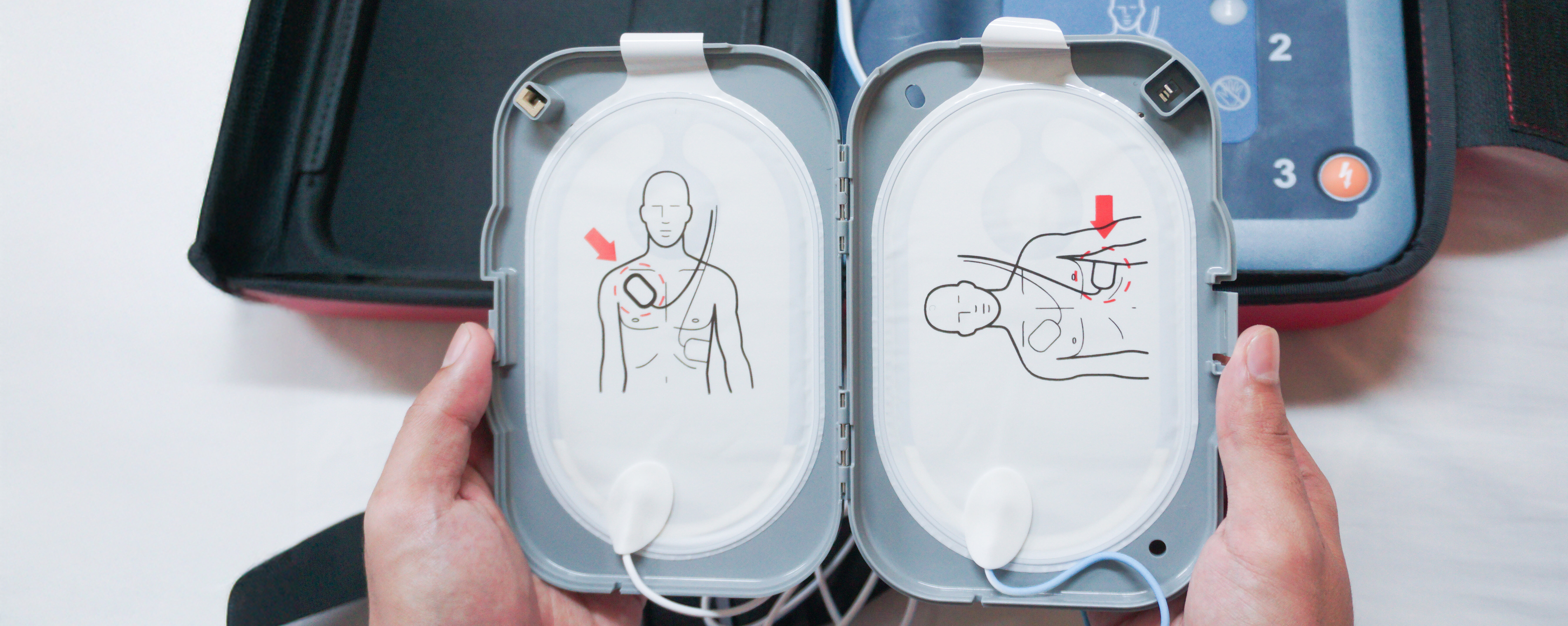 Tragbarer Defibrillator auf einem Holztisch, zwischen zwei Händen.