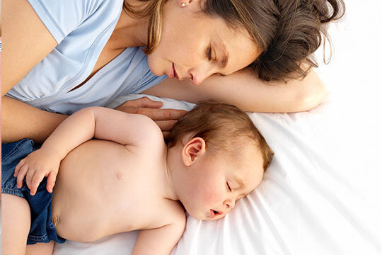Eine Mutter liegt mit ihrem Baby auf einem weißen Laken.