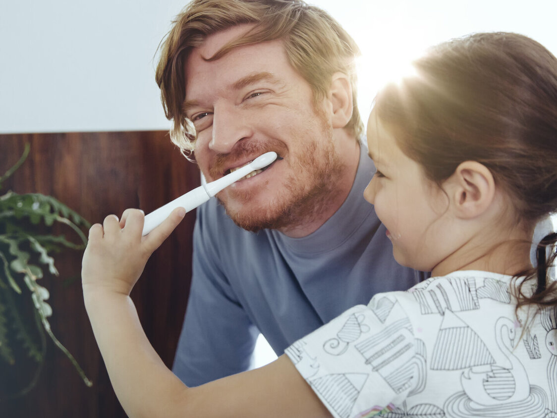 Ein Mädchen putzt einem Mann die Zähne.