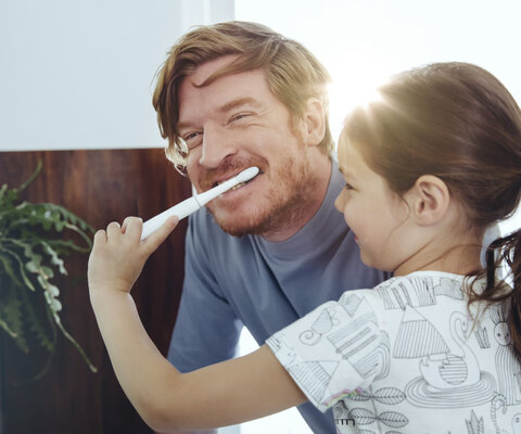 Ein Mädchen putzt einem Mann die Zähne.