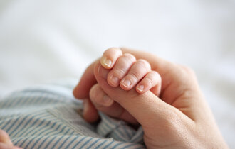 Ein Baby hält mit seiner Hand den Daumen eines Erwachsenen.