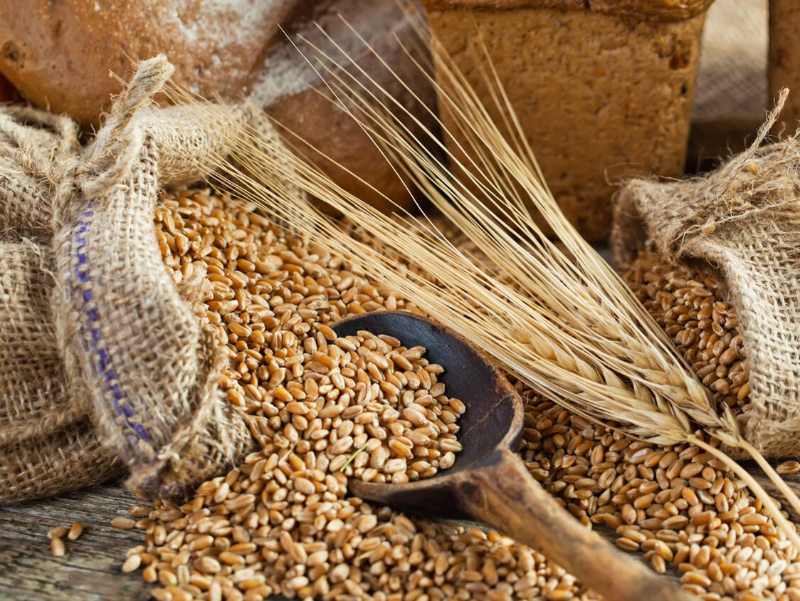 Verschiedene Getreidesorten in Säcken, dahinter Brot.