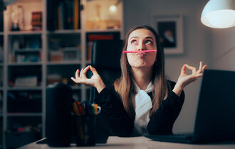 Frau im Büro balanciert Stift mit dem Mund und prokrastiniert.