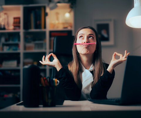 Frau im Büro balanciert Stift mit dem Mund und prokrastiniert.