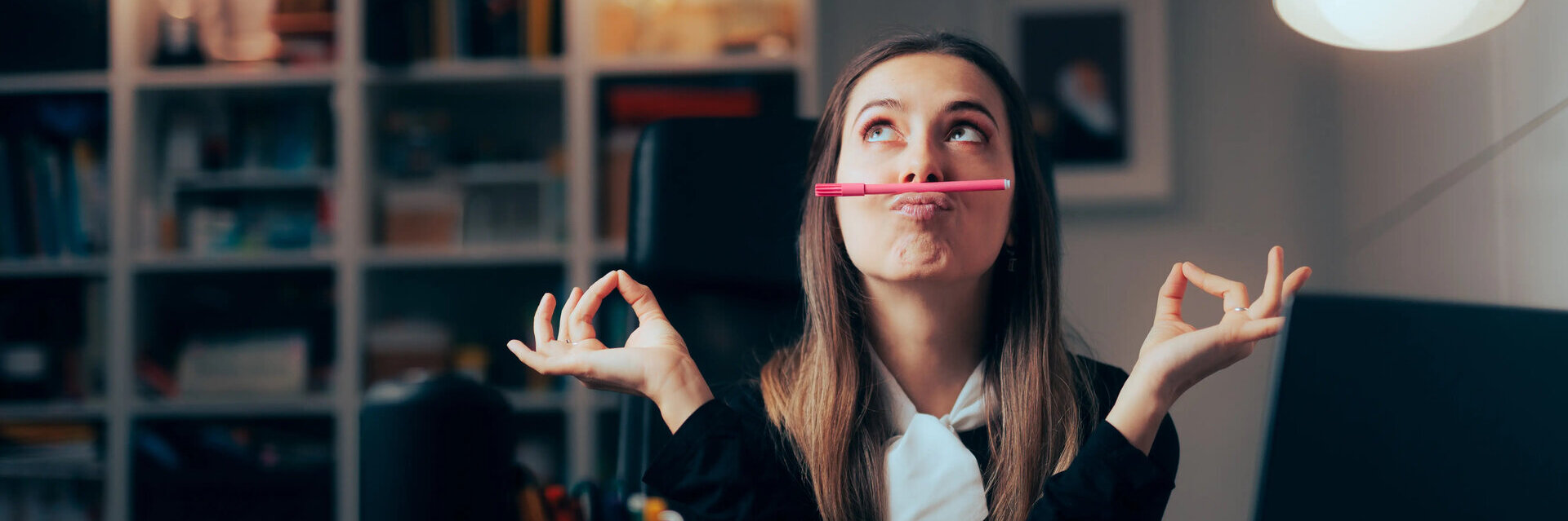 Frau im Büro balanciert Stift mit dem Mund und prokrastiniert.