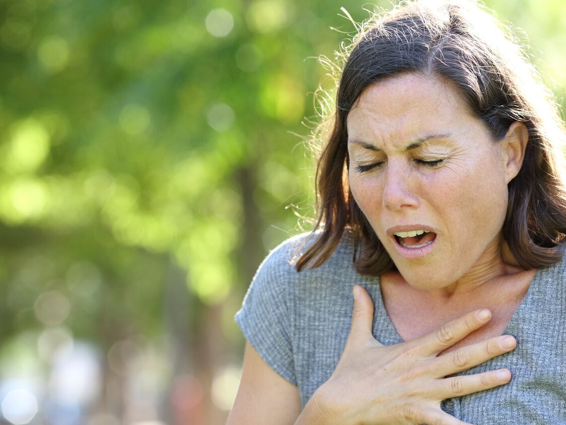 Eine Frau hält sich die Brust und hat hat Atemnot.