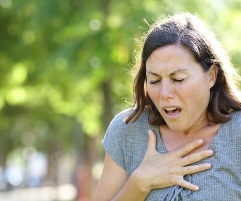 Eine Frau hält sich die Brust und hat hat Atemnot.