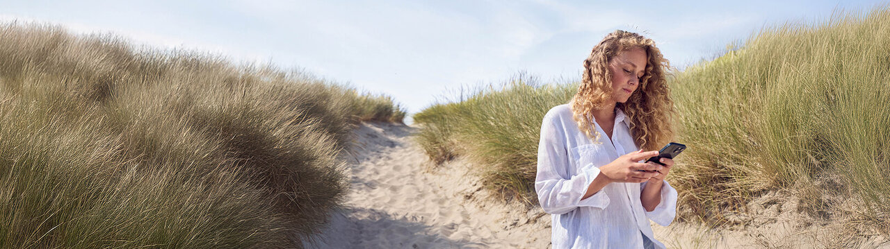 Eine Frau steht in einer Düne und guckt auf ihr Handy.