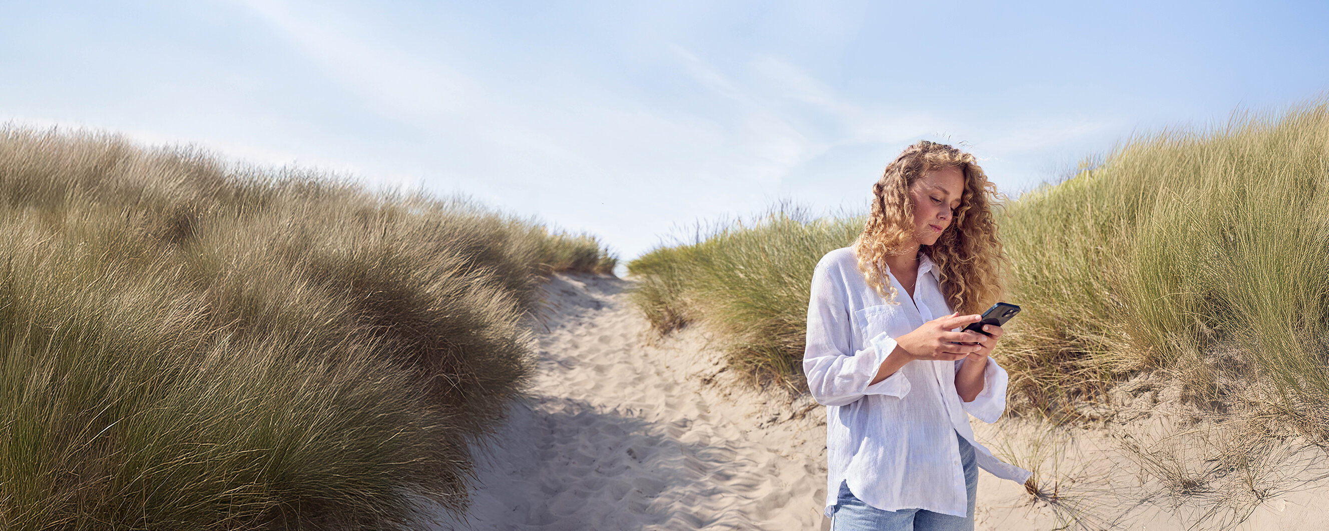 Eine Frau steht in einer Düne und guckt auf ihr Handy.