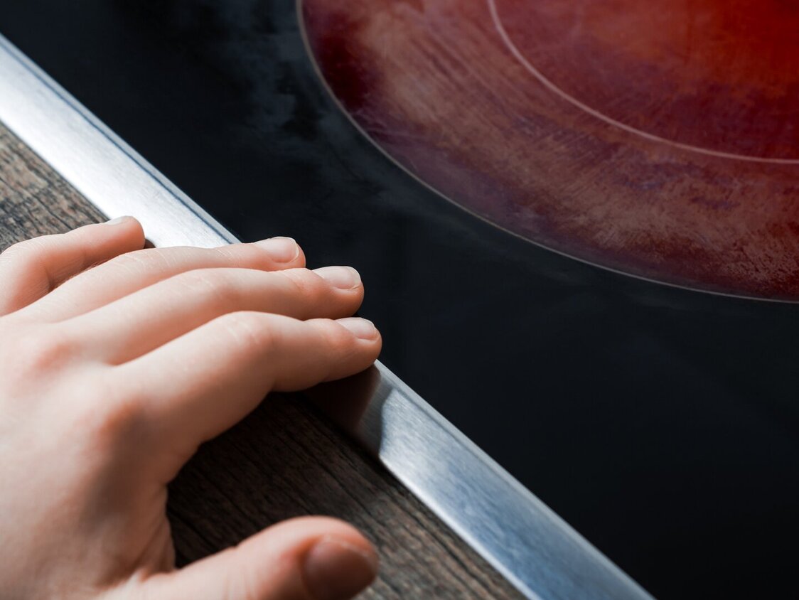 Das Foto zeigt eine rot-glühende Herdplatte. Kurz davor hat ein Kind seine Hand abgelegt.