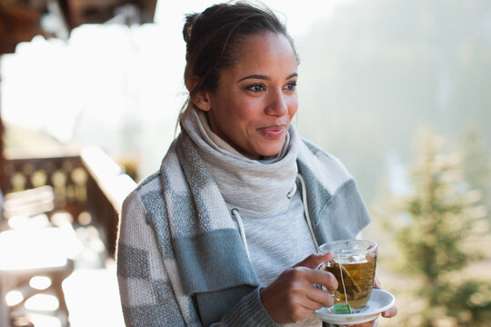 Eine lächelnde Frau trinkt draußen im Stehen einen Tee.
