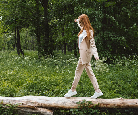 Eine Frau balanciert auf einem liegenden Baumstamm auf einer Waldlichtung. 