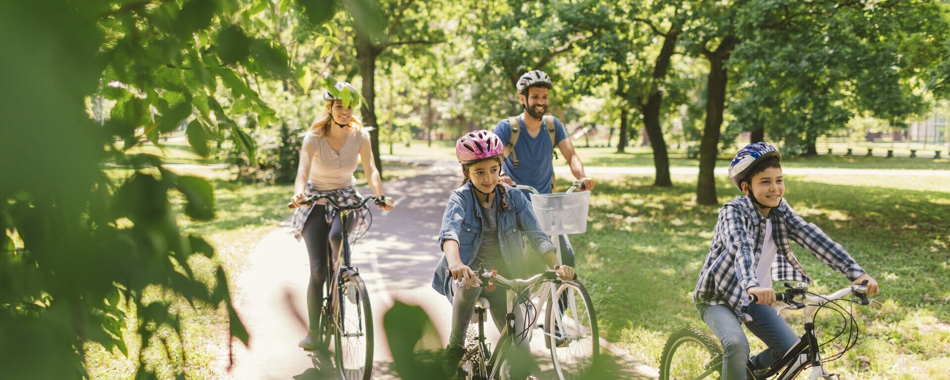 Eine vierköpfige Familie fährt durch einen Park mit vielen Bäumen.