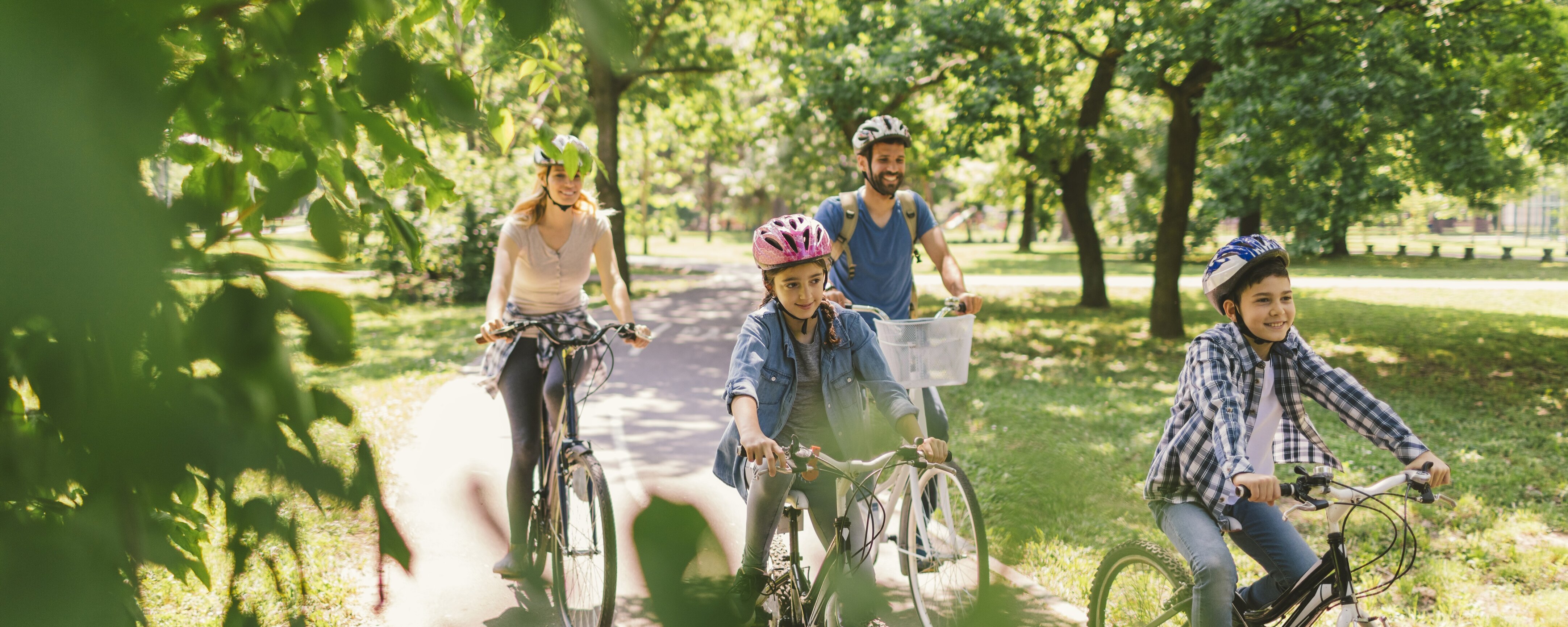 Eine vierköpfige Familie fährt durch einen Park mit vielen Bäumen.