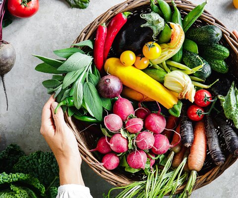 Ein runder Kord, der mit verschiedenem Gemüse gefüllt ist, steht auf einer Arbeitplatte.