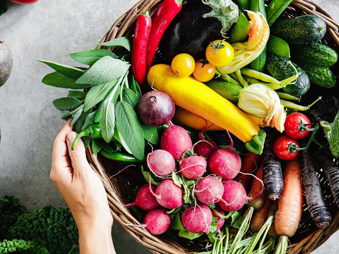 Ein runder Kord, der mit verschiedenem Gemüse gefüllt ist, steht auf einer Arbeitplatte.
