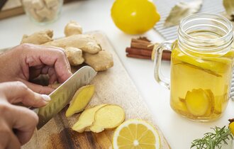 Hände, die auf einem Holzbrett Ingwer und Zitrone für ein Getränk zuschneiden.