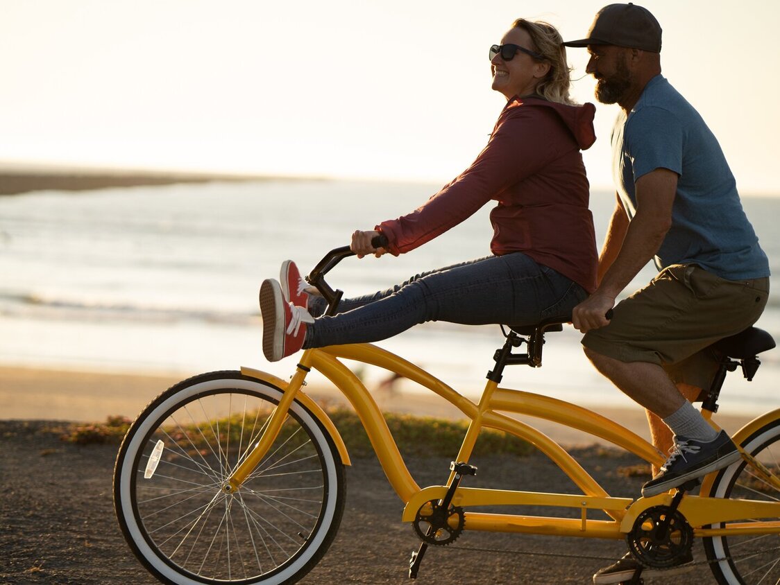 An einem Strand fährt ein Paar mit einem gelben Tandem an der Promenade entlang.