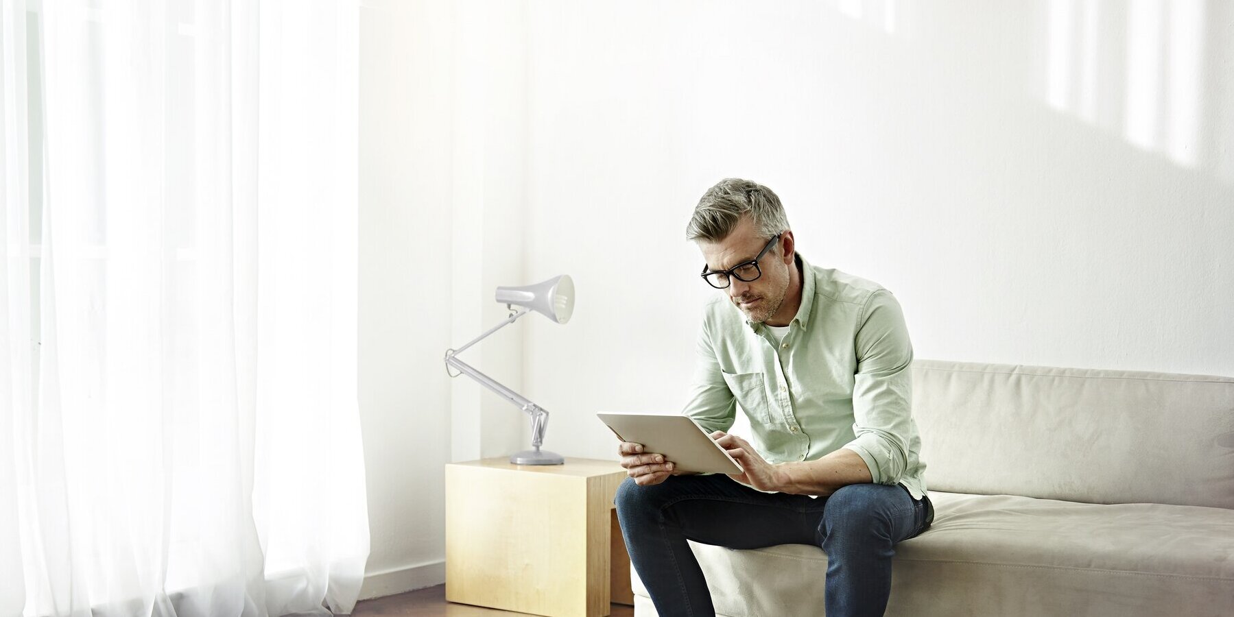 Ein Mann sitzt auf dem Sofa und nutzt ein Tablet.