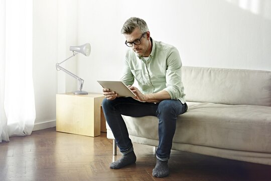 Ein Mann sitzt auf dem Sofa und nutzt ein Tablet.