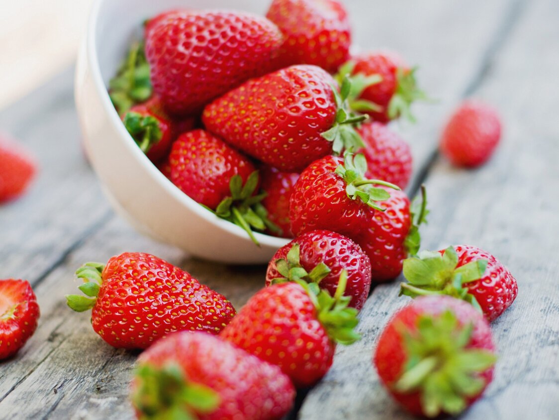 Eine Schale Erdbeeren, die umgekippt ist und einige Erdbeeren rausgefallen sind.