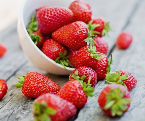 Eine Schale Erdbeeren, die umgekippt ist und einige Erdbeeren rausgefallen sind.