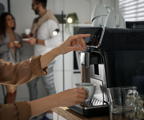 Eine Person holt sich einen Kaffee am Automaten.