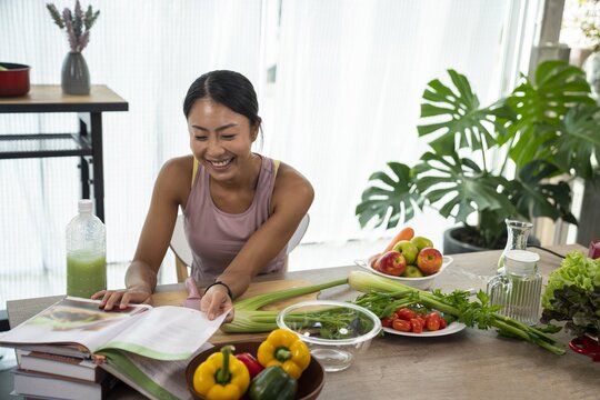 Eine asiatische Frau steht an einem Tisch mit einem aufgeschlagenen Kochbuch und drum herum liegt Gemüse.