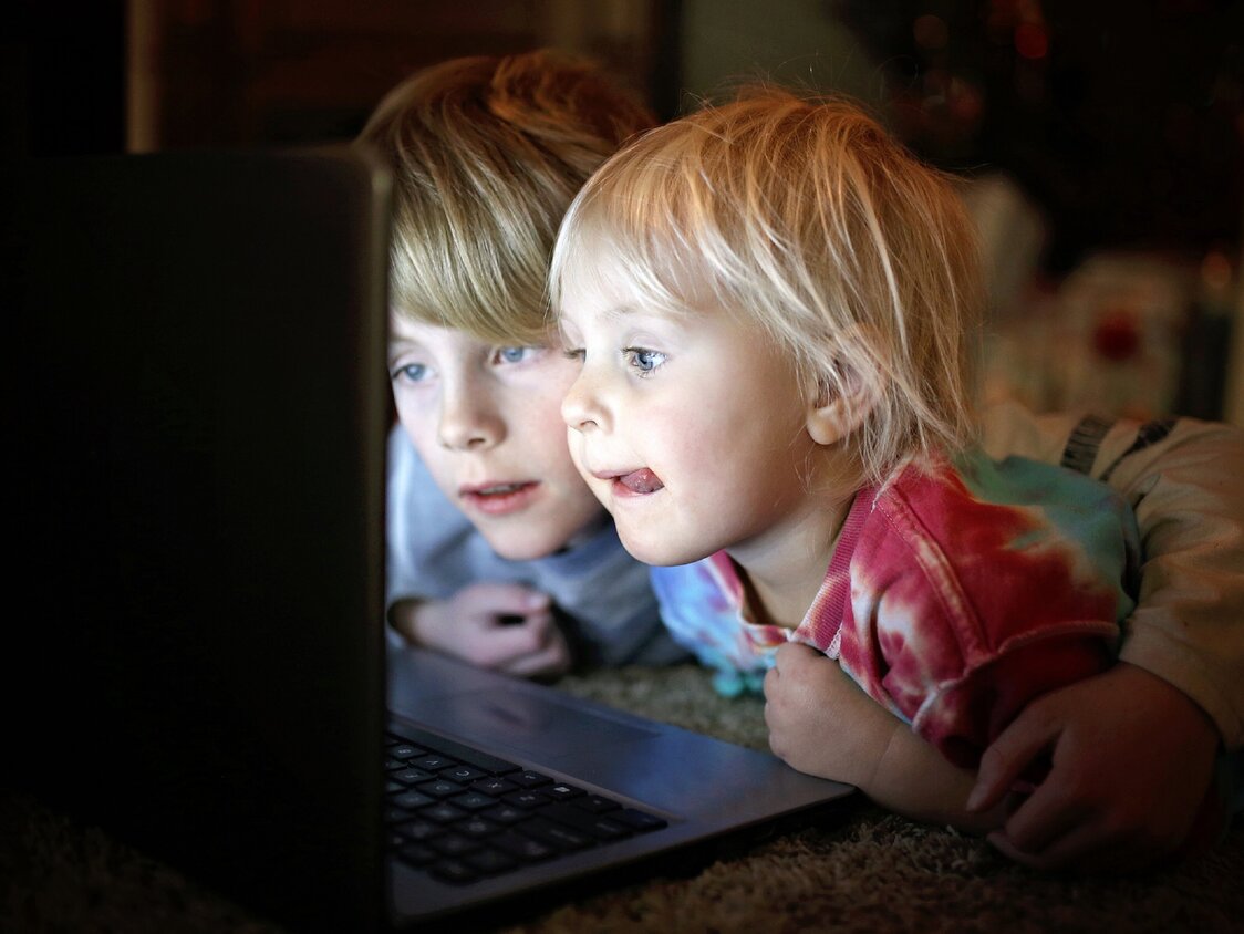 Zwei Kinder liegen bäuchlings auf dem Boden und gucken auf einen Laptop.
