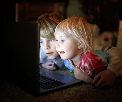 Zwei Kinder liegen bäuchlings auf dem Boden und gucken auf einen Laptop.