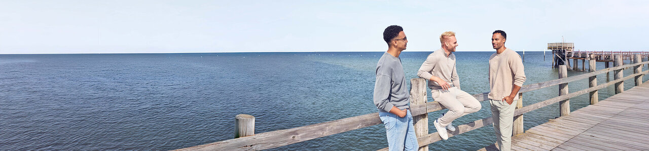 Drei Männer auf einem Steg am Meer.