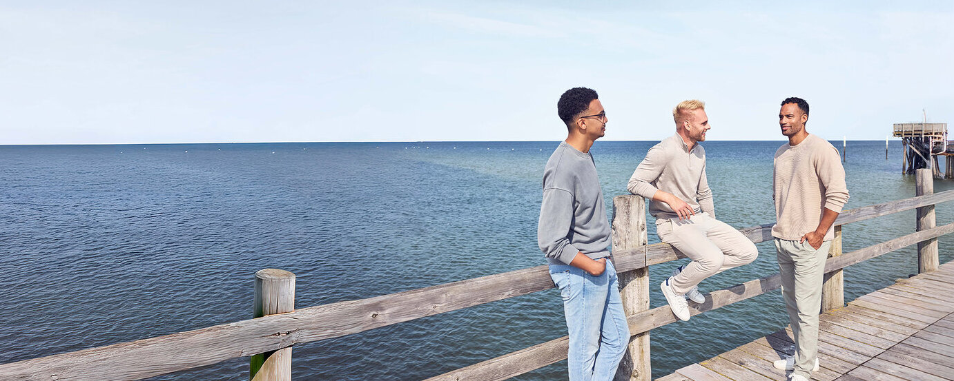Drei Männer auf einem Steg am Meer.