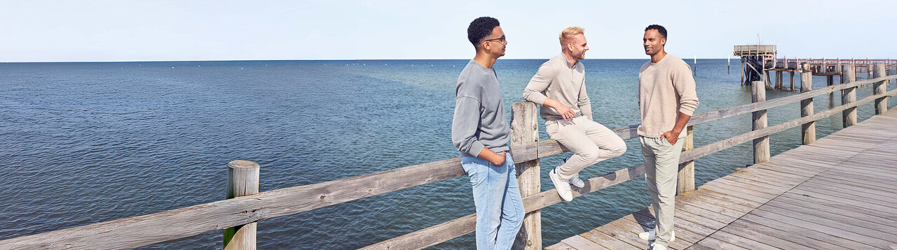 Drei Männer auf einem Steg am Meer.