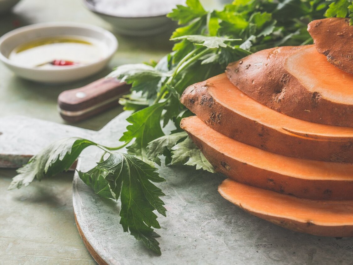 Eine geschnittene Süßkartoffel liegt auf einem Steinbrett.