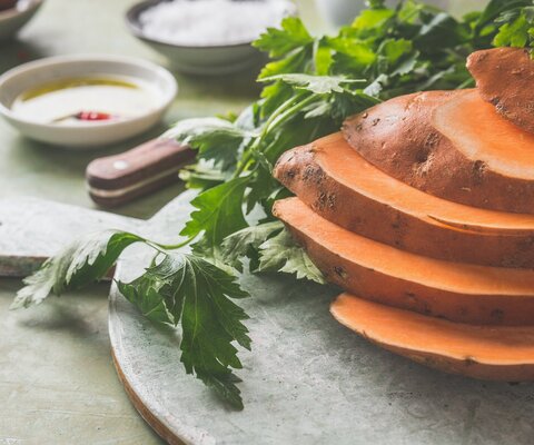 Eine geschnittene Süßkartoffel liegt auf einem Steinbrett.